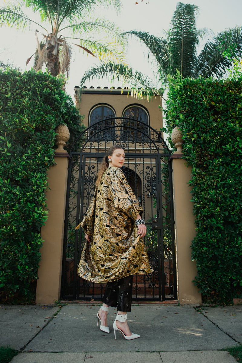 Girl in vintage Anthony Muto gold cocoon coat from Recess in front of gate